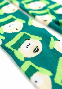 Calze verdi con volti di cartoni animati che indossano cappelli verdi, pelle bianca e occhi neri. Il tessuto ha un aspetto morbido e texturizzato con motivi ripetuti.