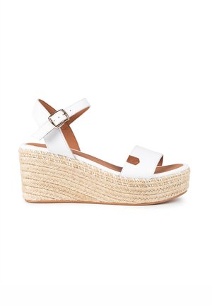 Sandalia de cuña blanca con suela de yute trenzada, dos correas anchas, correa de tobillo ajustable y textura suave y mate.