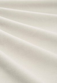 Elaśniany materiał w kolorze off-white z gładką powierzchnią, z subtelnymi wzorami tkanin i miękkimi fałdami. Idealny do różnych zastosowań tekstylnych.