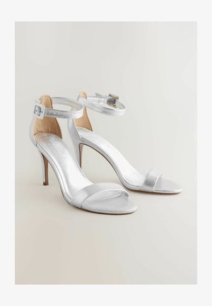 Srebrne sandale na visokih petah z naramnicami, ki se ponašajo z elegantnim dizajnom in sijočo končno obdelavo. Odprti prsti s tankim sprednjim trakom in stiletto peto.