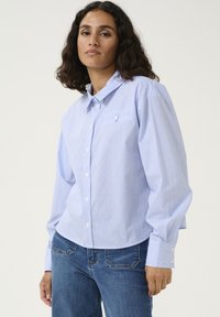 Gestreepte blauwe overhemd met kraag en een enkele borstzak, gecombineerd met strakke blauwe jeans. Geweven stof met witte knoopaccenten.