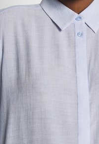 Camicia blu chiaro con bottoni, con una finitura testurizzata, dotata di un colletto classico, sottili righe verticali e bottoni blu chiaro.