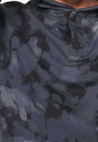 Kapuzensweatshirt aus dunklem, strukturiertem Stoff mit einem abstrakten Camouflage-Muster in Schwarz, Grau und Blau. Dreiknopfverschluss am Hals.