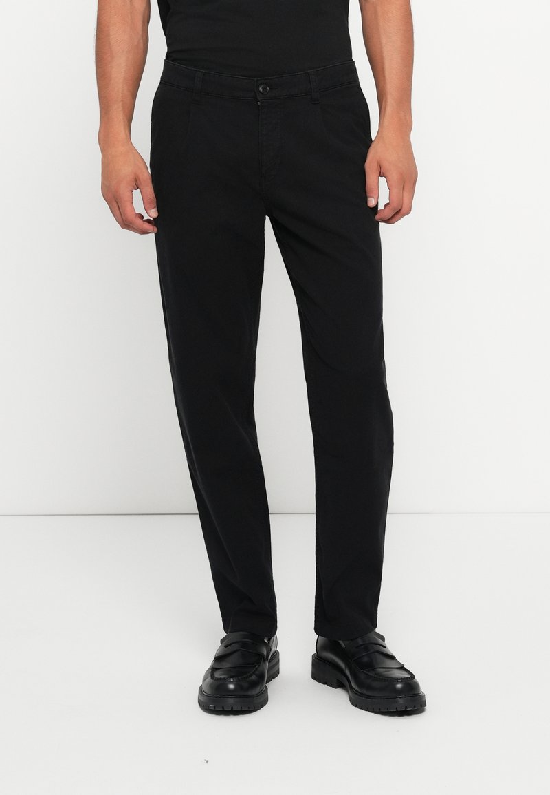 Black chinos with a tailored fit, featuring a button closure, side pockets, and a smooth texture. Worn with black slip-on shoes.