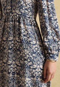 Tumedane lilleline kleit puuvilla segust, kogutud vöökohaga, pikad varrukad ja valged lillemustrid; omaduseks on peen cuffs'i disain.