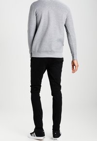 Gray sweatshirt with crew neck and ribbed hem, paired with black slim-fit pants. Footwear features black and white striped accents.
