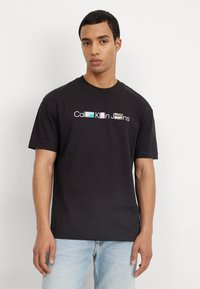 Camiseta de algodón negra con un logo gráfico de texto multicolor "Calvin Klein Jeans" en la parte frontal. Mangas cortas y un diseño clásico de cuello redondo.