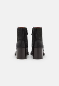 Botas de tobillo de cuero negro con un acabado suave, que presentan un tacón de bloque sólido y cierre de cremallera, vistas desde la parte posterior.