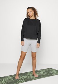 Sweatshirt preto de mangas longas com um corte descontraído, combinado com calções de ciclismo cinza claro. Pose de corredor em um tapete de yoga com padrão verde.