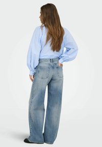 Camisa azul clara de gran tamaño con mangas abullonadas, combinada con jeans de tiro alto y corte holgado en denim azul medio desgastado.
