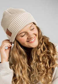 Beżowa dziana czapka z poziomymi prążkami, z prostokątną skórzaną metką. Miękka faktura i składany design.