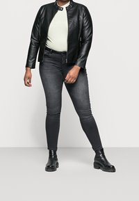 Giacca in pelle nera con colletto rialzato, top verde chiaro, jeans skinny scuri e stivaletti neri con suola spessa.