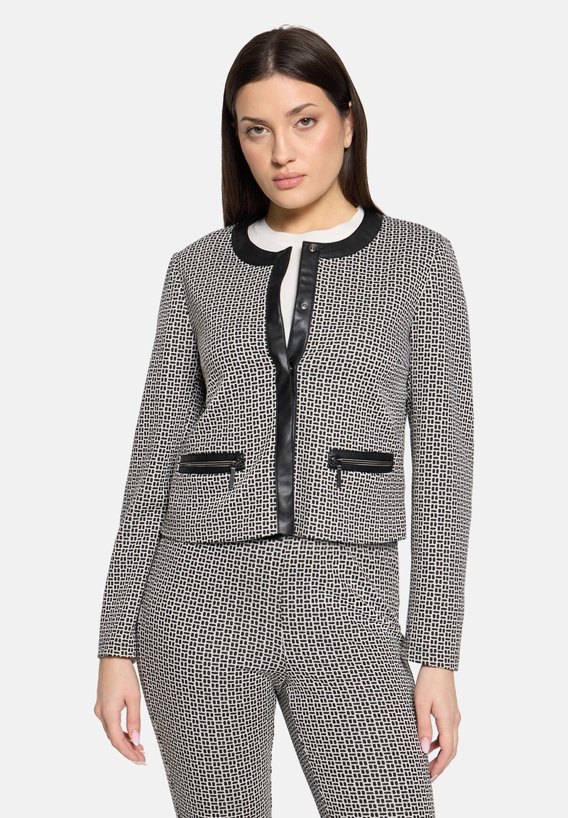 Veste noire et blanche avec un motif quadrillé texturé, bordure noire, deux poches avant et coupe courte. Boutons sur le devant.