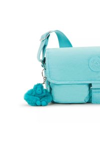 Turquoise crossbody bag with flap closure, featuring a textured surface and a furry turquoise gorilla keychain attachment.