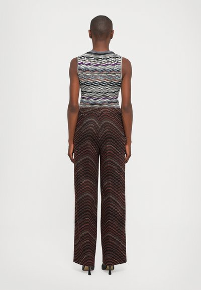 Persona che indossa un top senza maniche con un motivo a zigzag multicolore e pantaloni a gamba larga con un motivo a zigzag simile, in piedi di spalle su sfondo bianco.