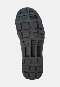 Schwarze Gummisohle mit strukturiertem Design, featuring geriffelte Muster und einem grünen Akzent. Größe markiert als 42.