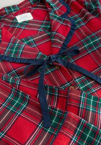 Rotkariertes Schlafanzug-Oberteil mit Marineblauem Saum, ausgestattet mit Knöpfen und einer Schleifen-Applikation. Weicher Stoff mit klassischem Tartan-Muster in Grün- und Weißakzenten.