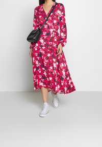 Abito midi floreale con maniche lunghe nei colori rosa, rosso e blu navy. Abbinato a sneakers bianche e una piccola borsa a tracolla nera.