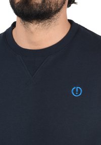 Navy blue sweatshirt with round neck, ribbed cuffs, and hem. Features a small blue logo accent on the chest and soft texture.