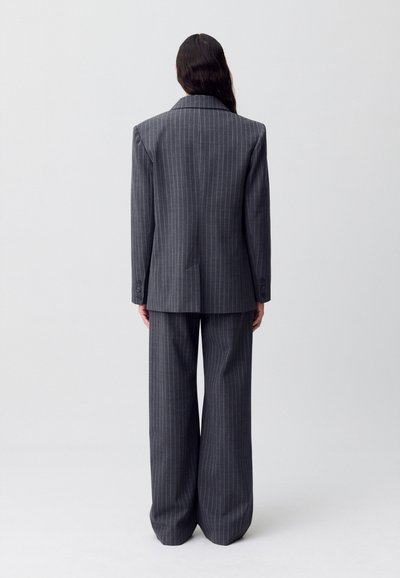 Traje gris a rayas con un blazer estructurado que incluye hombreras y pantalones de pierna ancha, fabricado con una textura suave.