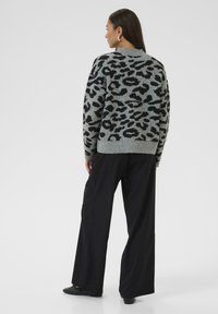 Grey sweater with black leopard print design, round neckline, and ribbed hem. Paired with wide black trousers and simple black footwear.