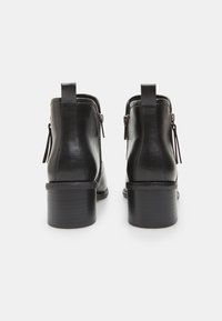 Botines de cuero negro con una textura suave, cremalleras laterales y un tacón cuadrado. Presentan una tira en la parte trasera para facilitar su puesta.