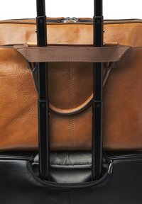Brown leather briefcase secured on a black rolling suitcase handle with a fabric strap, showing zipper and telescopic handle.