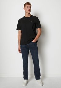 Camiseta de algodón negra con mangas cortas y un pequeño logo en el pecho, combinada con jeans de mezclilla azul oscuro y zapatillas blancas.