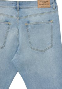 Jeans in denim azzurro chiaro con una texture sbiadita, dotati di due tasche posteriori e cuciture gialle. Include un'etichetta in pelle con il marchio in vita.