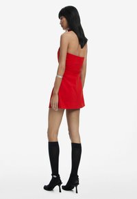 Red strapless mini dress with a fitted bodice, flared skirt, and smooth fabric. Paired with black knee-high socks and heeled shoes.