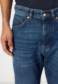 Mørkeblå denimjeans med vanlig passform, med oransje søm, en frontlomme og en metallknapp-lukking i midjen.