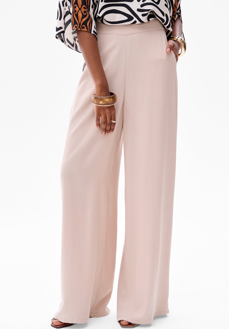 Lichtroze wijde broek van gladde stof, met een hoge taille en zijzakken, gedragen met een met patroon bedrukte top en accessoires.