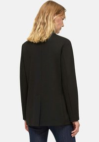 Blazer nero su misura con design strutturato, spacco singolo sul retro e maniche lunghe. Tessuto strutturato, stile minimalista.
