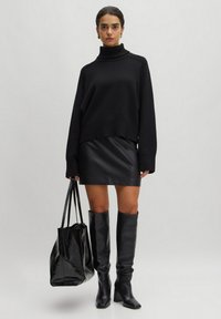 Zwarte gebreide coltrui, hoog-waist leren minirok, kniehoge glanzende zwarte laarzen en een grote zwarte handtas.