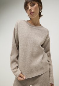 Beiger Strickpullover mit rundem Ausschnitt, geripptem Saum und überschnittenen Schultern. Verfügt über eine weiche Textur und einen lässigen Schnitt.