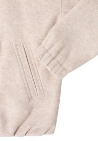 Jasnoróżowa tkanina o teksturowanej powierzchni i miękkim wykończeniu, z prążkowanym mankietem oraz boczną kieszenią ozdobioną pionowymi przeszyciami.