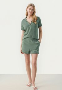 Grøn terrycloth sæt bestående af en kortærmet polo skjorte og shorts med elastisk talje, begge med en afslappet pasform og subtil tekstur.