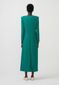 Abito lungo teal con maniche lunghe, dalla texture liscia, spalline e zip sul retro, dotato di uno spacco centrale sull'orlo.