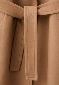 Lichtbruine stoffen riem met een gladde textuur en een knoopdetail. De riem maakt deel uit van een kledingstuk gemaakt van een zacht, warm materiaal.