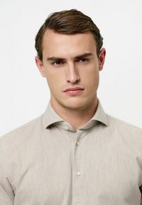 Camisa beige claro con botones, fabricada con un tejido texturizado, que presenta un cuello clásico y sutiles rayas verticales. Acabado liso y corte entallado.