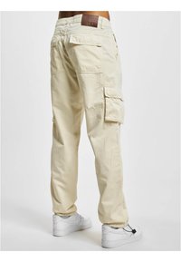 Beige cargobroek van katoen, voorzien van zijzakken, een leren label in de tailleband en een comfortabele pasvorm. Gecombineerd met witte sneakers.