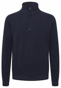 Pull-over à col zippé bleu marine en tissu texturé ; il est doté de manches longues, de poignets côtelés et d'un petit logo au bas.