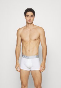 Beli pamučni bokserice sivoj Calvin Klein logo elastičnom pojasu, prilagođeni dizajn i meka tekstura, nosi muški model.