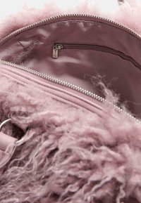 Indersiden af en pink pels taske med blødt stoffor. Har en lynlåslomme og sølvhardware. Den teksturerede pels tilføjer dybde.