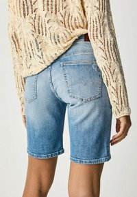Bermudas de denim en azul claro con un acabado desgastado, que cuentan con un diseño de cinco bolsillos y detalles cosidos en los bolsillos traseros.