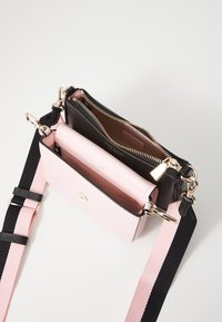 Crossbody bag with a pink leather exterior and black interior, featuring gold hardware, zip closures, and a striped adjustable strap.