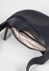 Borsa a spalla in pelle nera con una superficie liscia, chiusura con zip e una foderatura strutturata di color crema con un motivo geometrico.