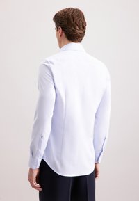 Camicia bianca a maniche lunghe con una texture sottile, colletto a punta e orlo arrotondato. Presenta polsini con bottone e un design attillato.