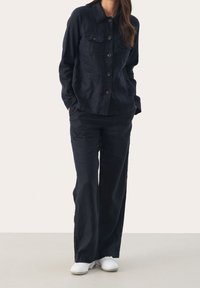 Chaqueta de lino navy con cierre de botón y dos bolsillos en el pecho, combinada con pantalones de pierna ancha. Ambos artículos tienen un acabado texturizado.