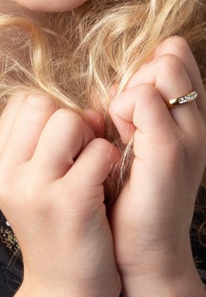 Gouden ring met een glanzend oppervlak en ingelegde stenen, gedragen aan een hand die lange, golvende, blonde haren vasthoudt, met een mooie huidstructuur.